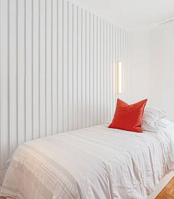 Vista de uma cama de solteiro com uma parede com ripas de madeira pintadas de branco